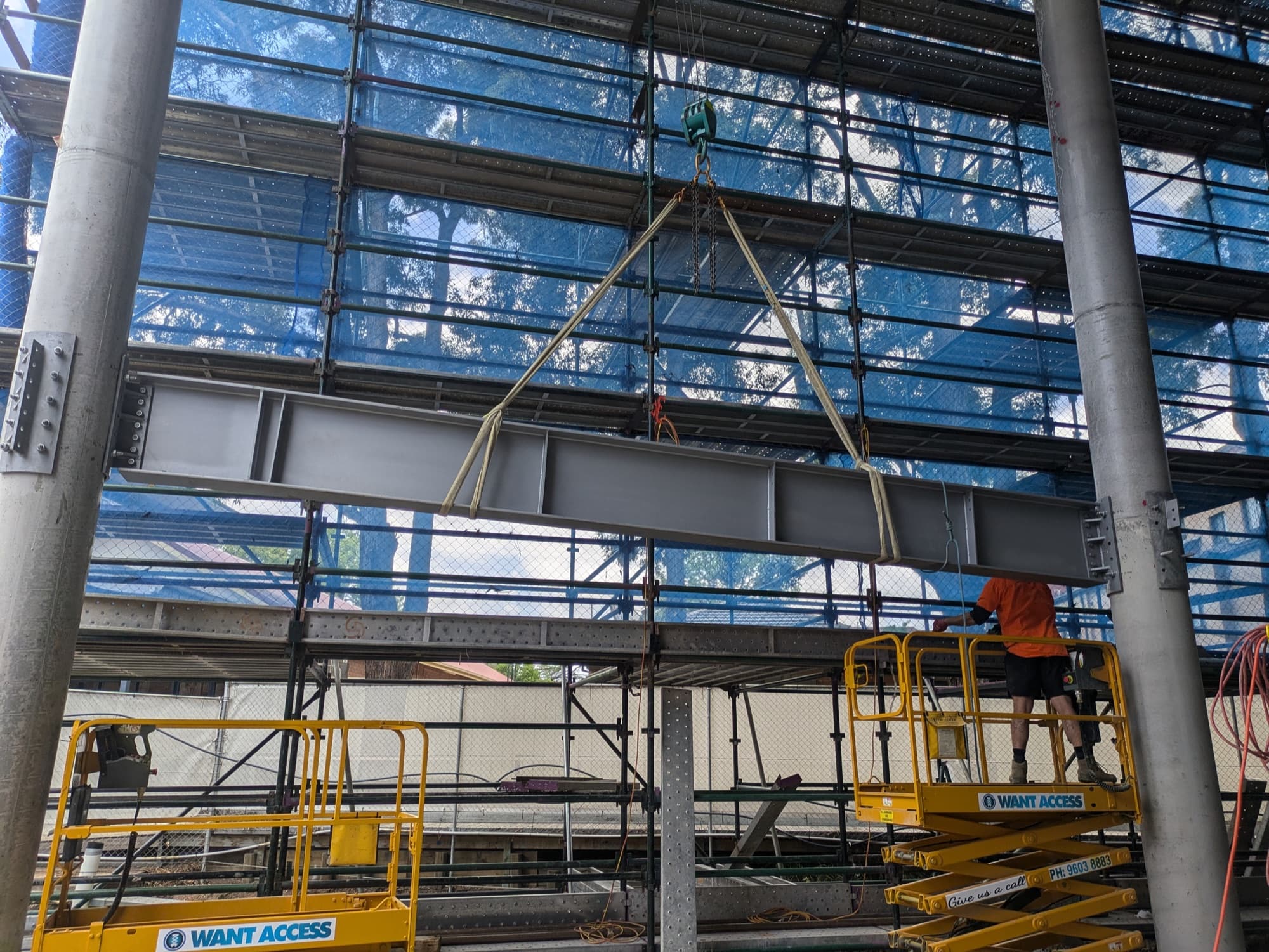 Steel beams and columns going up behind scaffold, spider crane on site, Strathfield